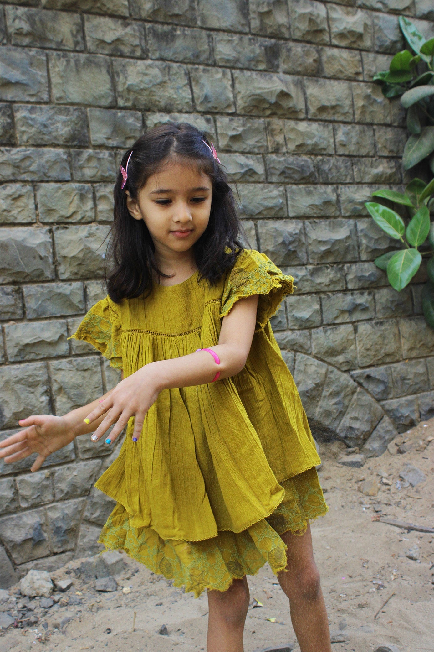 Front view of a golden yellow flutter dress for kids, crafted from lightweight cotton with soft gathers at the waist and delicate flutter lace sleeves. Features a back button fastening and a breezy, relaxed shape for everyday wear.